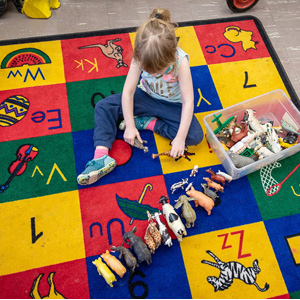 A child sits on a colorful play mat with toy animals lined up in a single row.