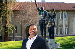 Black male in suit in front of Victory statue at SJSU