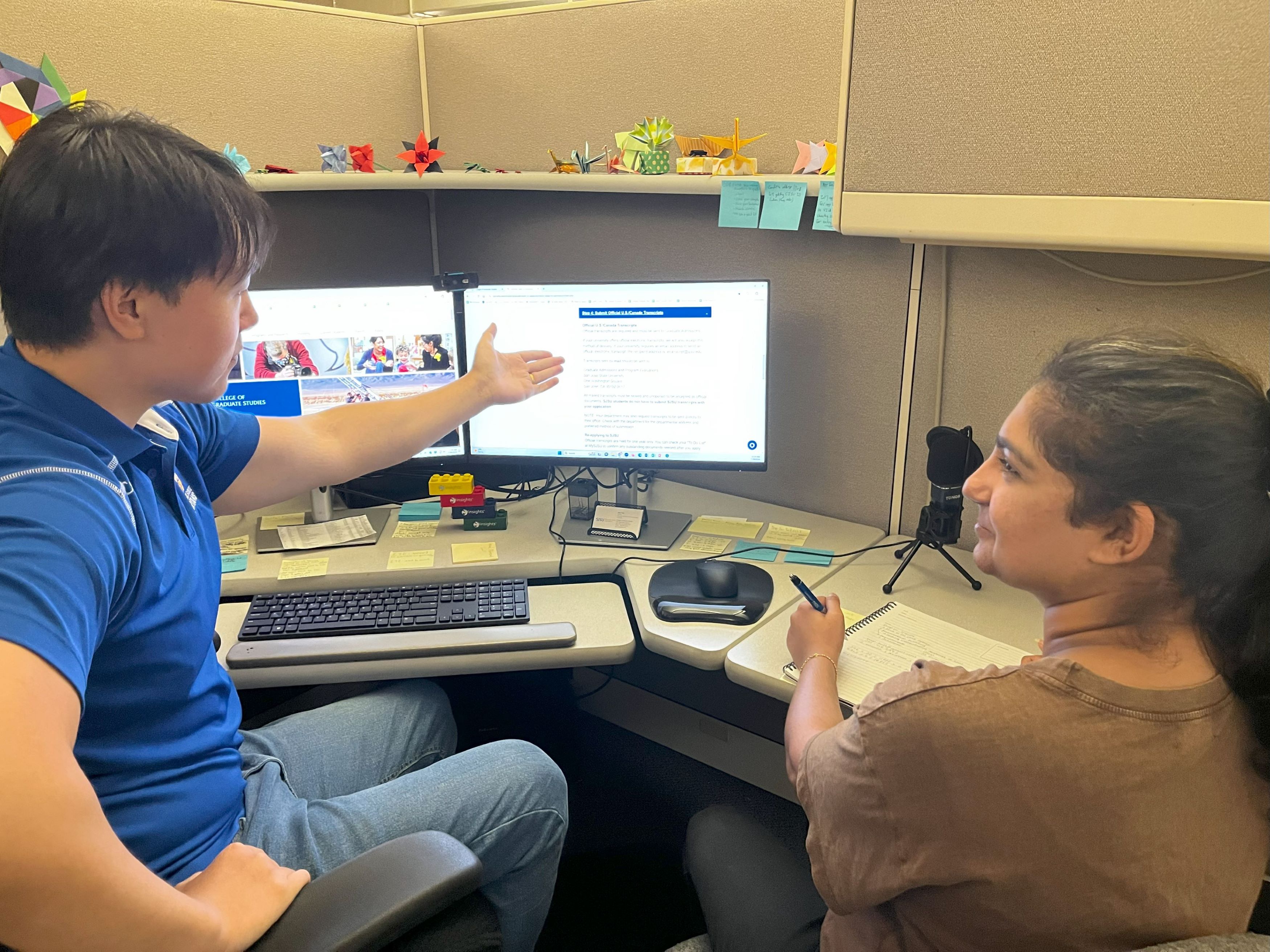 counselor advising student in cubicle, counselor gesturing to screen while student looks at screen