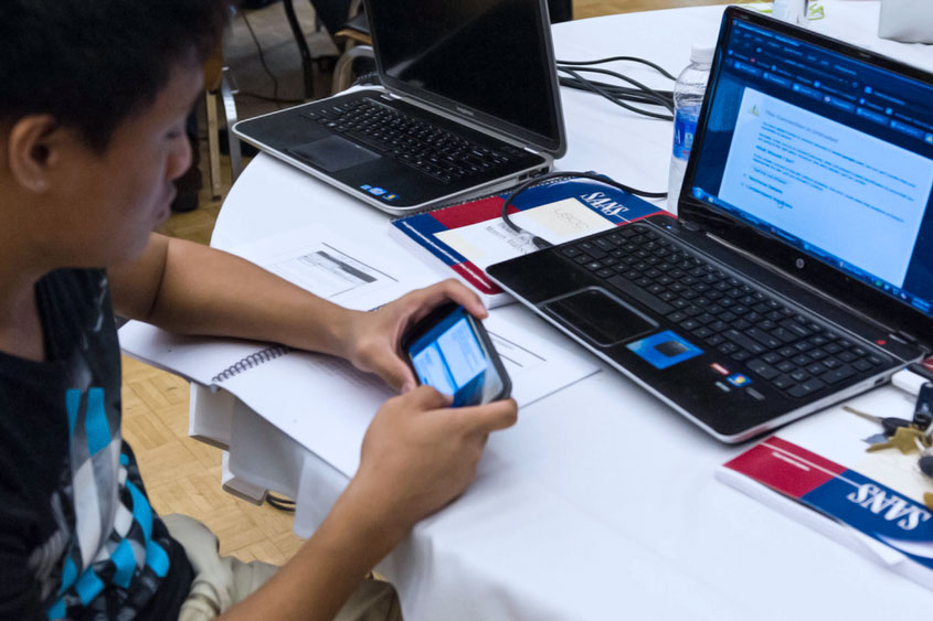 Student holding a mobile phone connected to laptop.