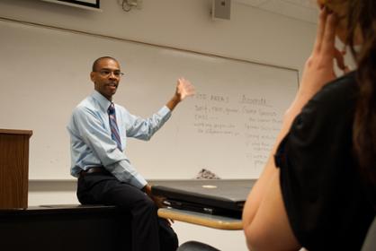 Instructor gestures towards whiteboard in his classroom