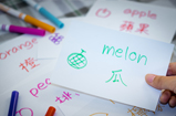 a thumb of a person holding an index card with green writing on the card with crayons in the background. 