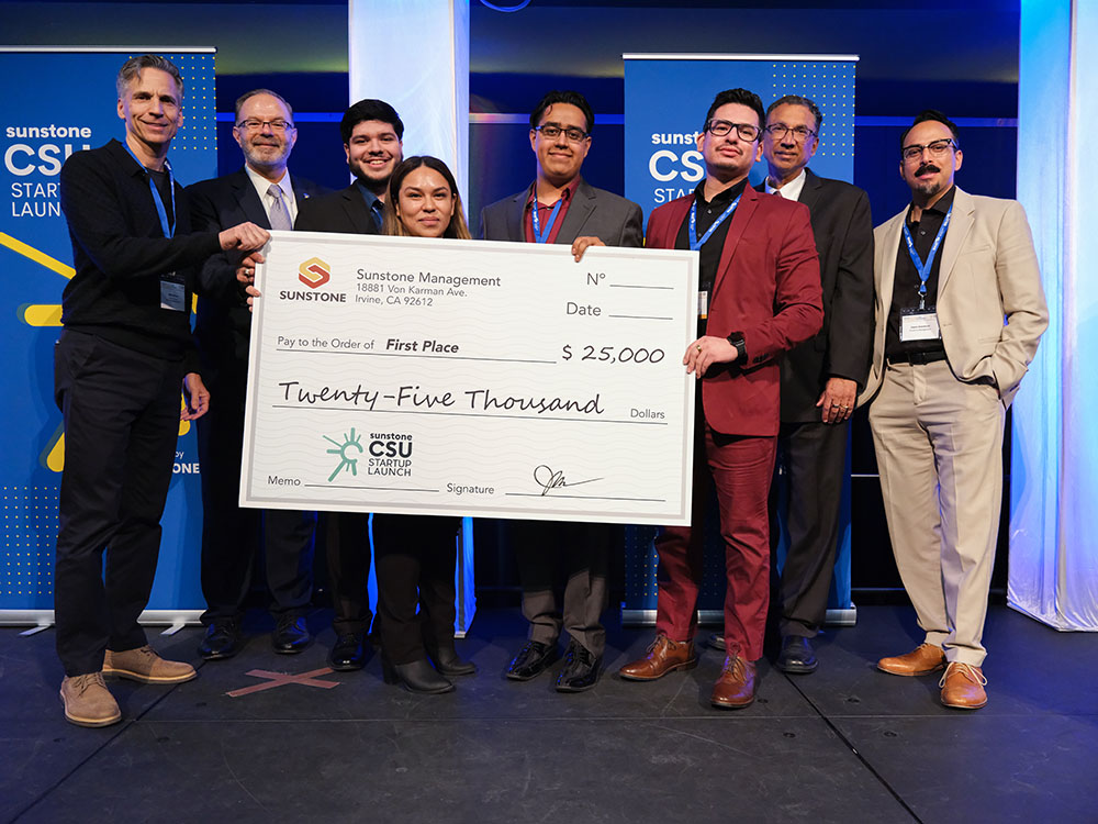 Four college-age startup founders pose onstage with two sponsors, two hosts, and a giant check for $25,000