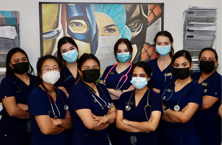 BSN students stand in front of a poster which depicts comic book heroes, with a nurse standing with them.