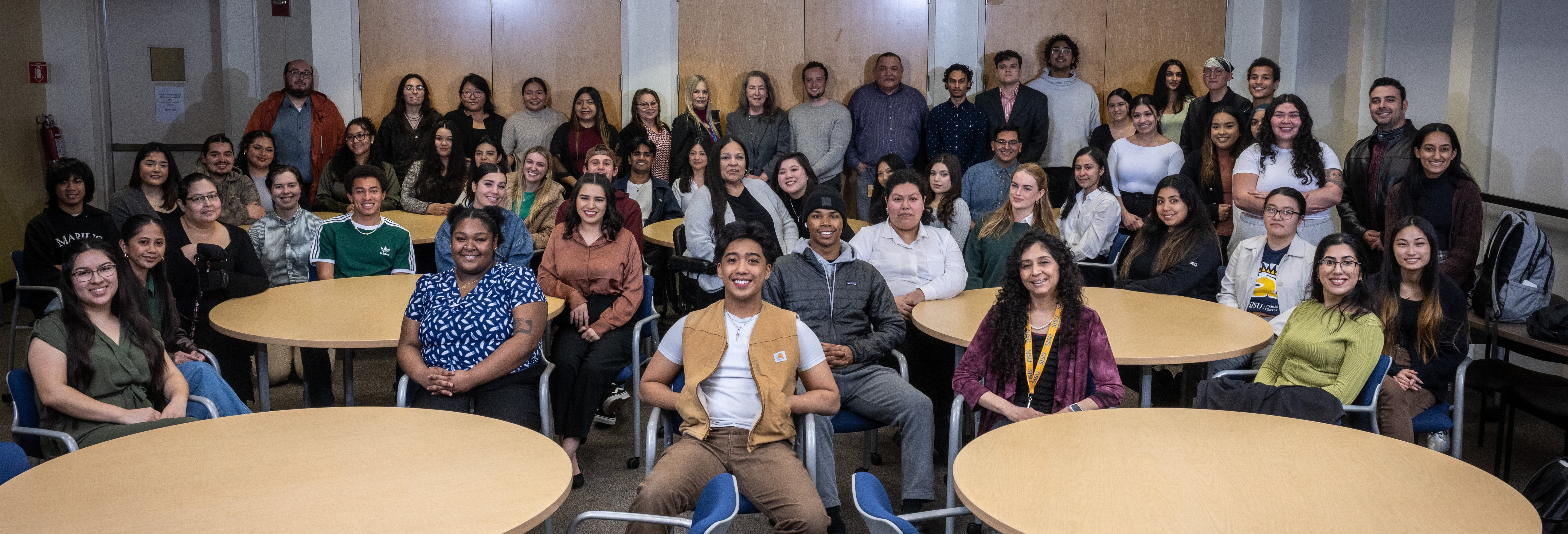 Group of students and a professor, in formal attire, pose for a classroom photo.