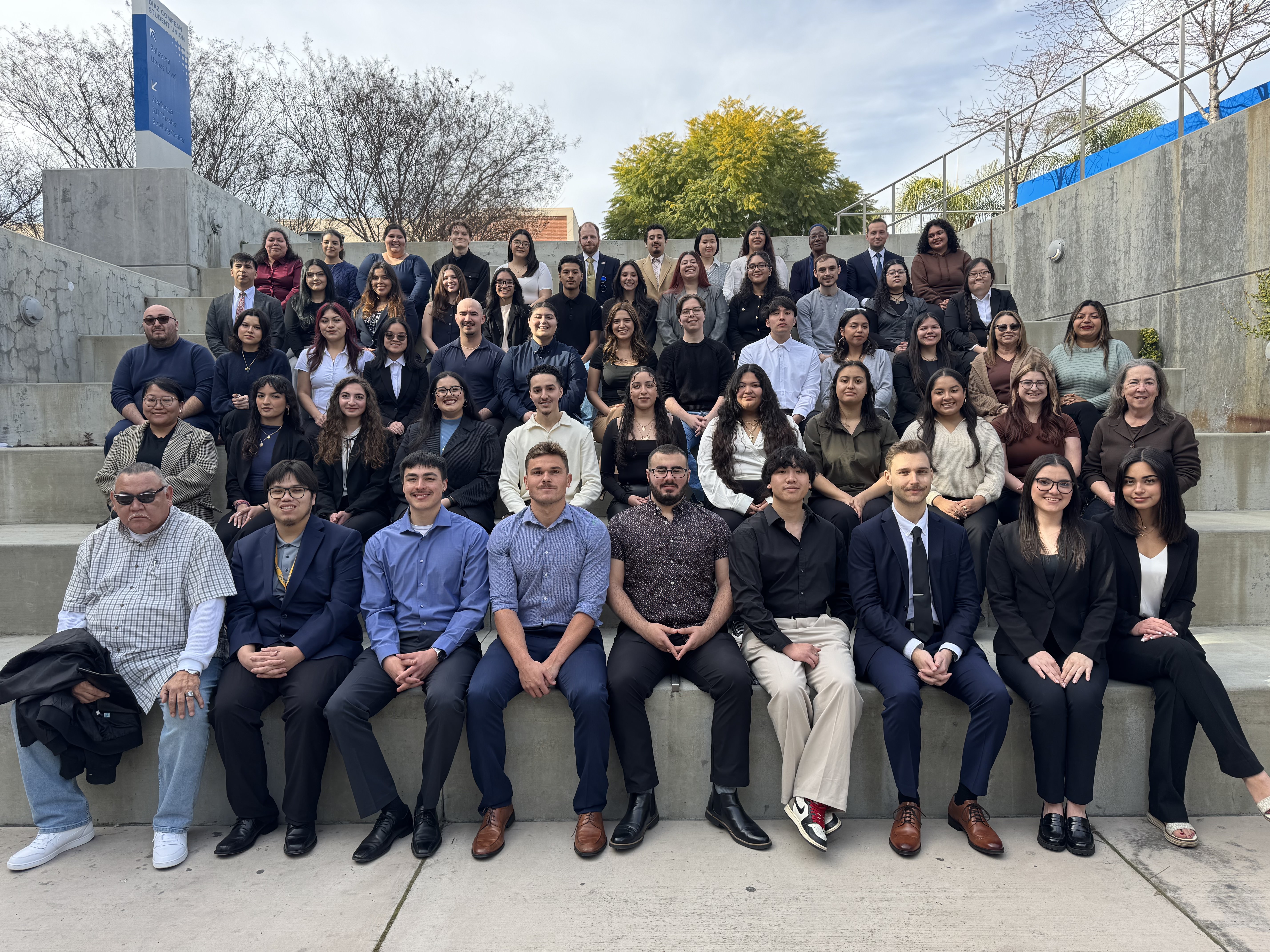 Group of students and a professor, in formal attire, pose for a classroom photo.