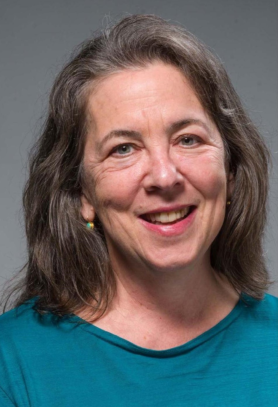 white female attorney with long, brown hair, dressed in a blue dress-shirt, smiling in front of a gray background