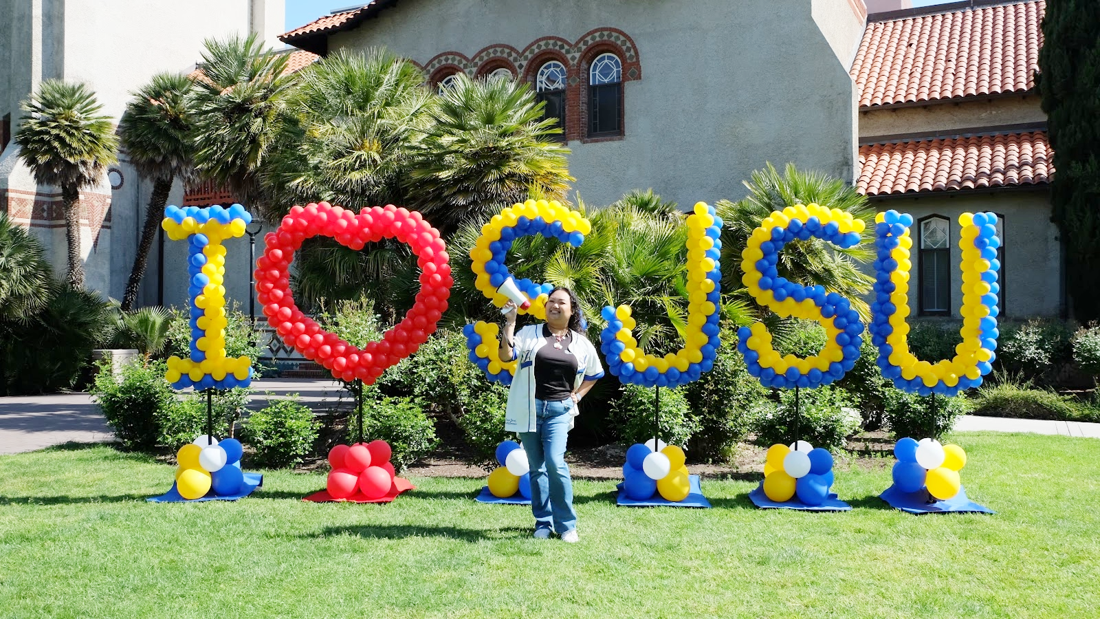 Person with megaphone posed in from of I love SJSU balloon formation