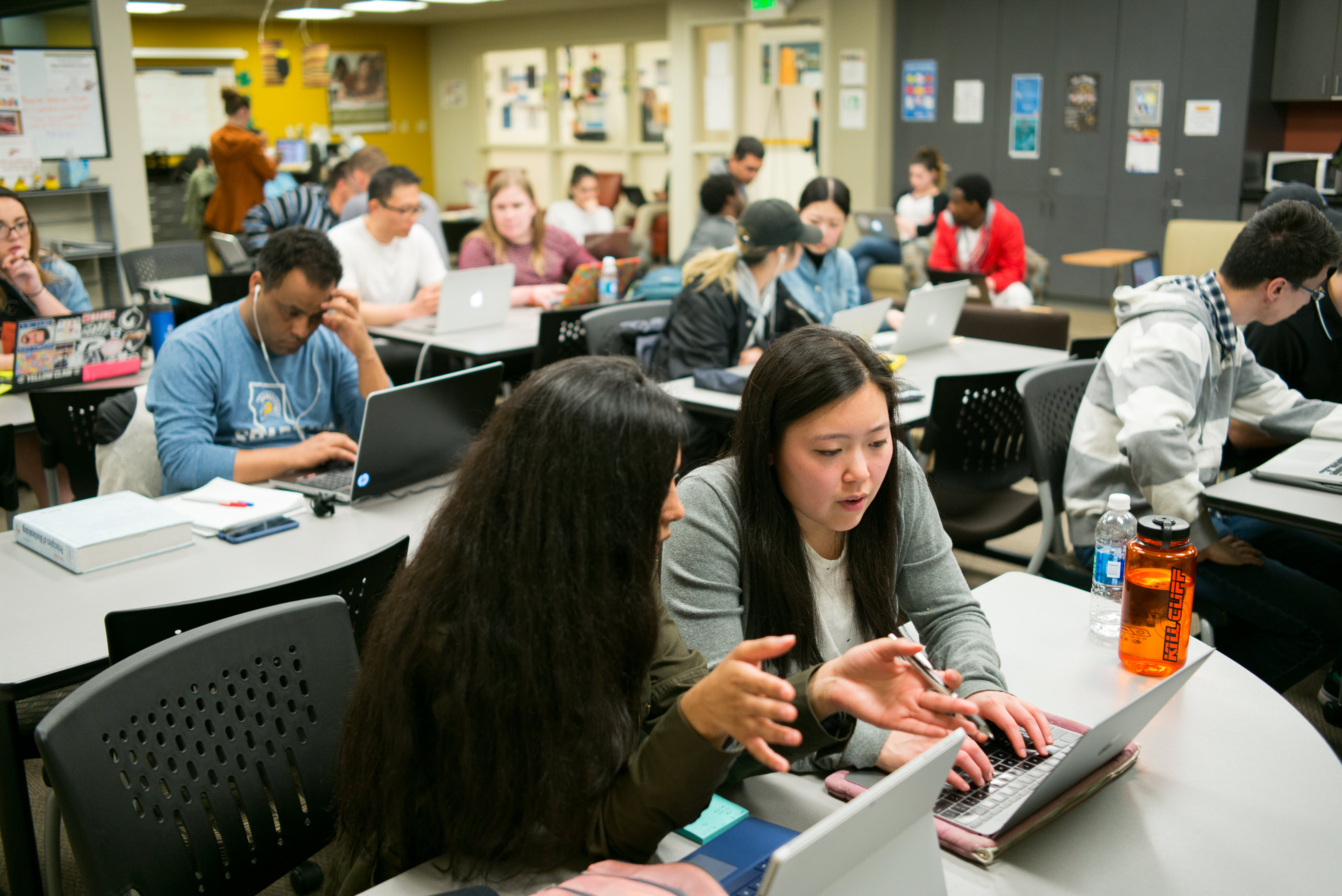 Students sit in a classroom looking at laptop computer while working together.