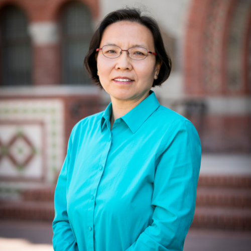 headshot of lixia hou in turquoise shirt with tower hall entrance in background